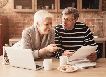 Pareja de adultos mayores sonriendo leyendo documentos legales en la cocina